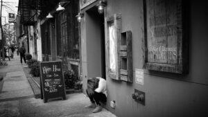 Dejected person sitting on the stoop of a bar, next to a happy hour sign. 2015. Manhattan. New York City. © Amha Mogus